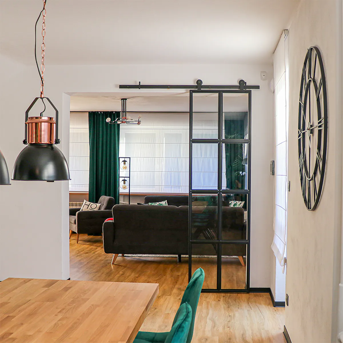 Black metal wall clock, industrial style clock, loft décor, metal glass door, loft door, metal glass sliding door, black glass door, green dining chairs, open living room to dining room, industrial pendant lights for dining room, large wooden dining table