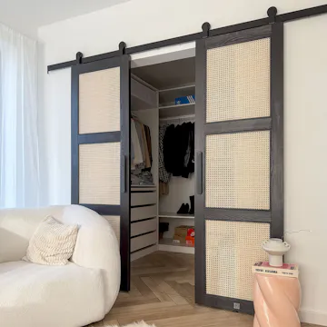 intérieur de chambre moderne avec portes coulissantes ouvertes en rotin noir révélant une armoire minimaliste et un fauteuil texturé blanc