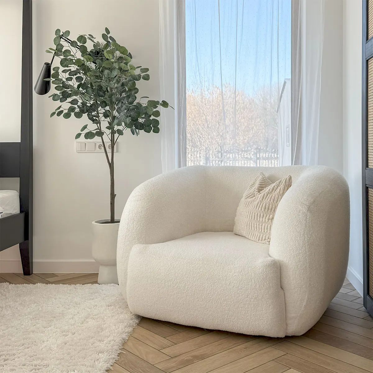 un fauteuil blanc confortable avec un coussin texturé se trouve à côté d'un tapis blanc doux et d'une plante en pot