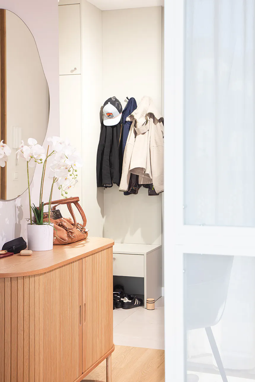 Entry hallway with wooden dresser, round mirror, white orchids, clothing rack and shoe cabinet partially visible through white sliding doors