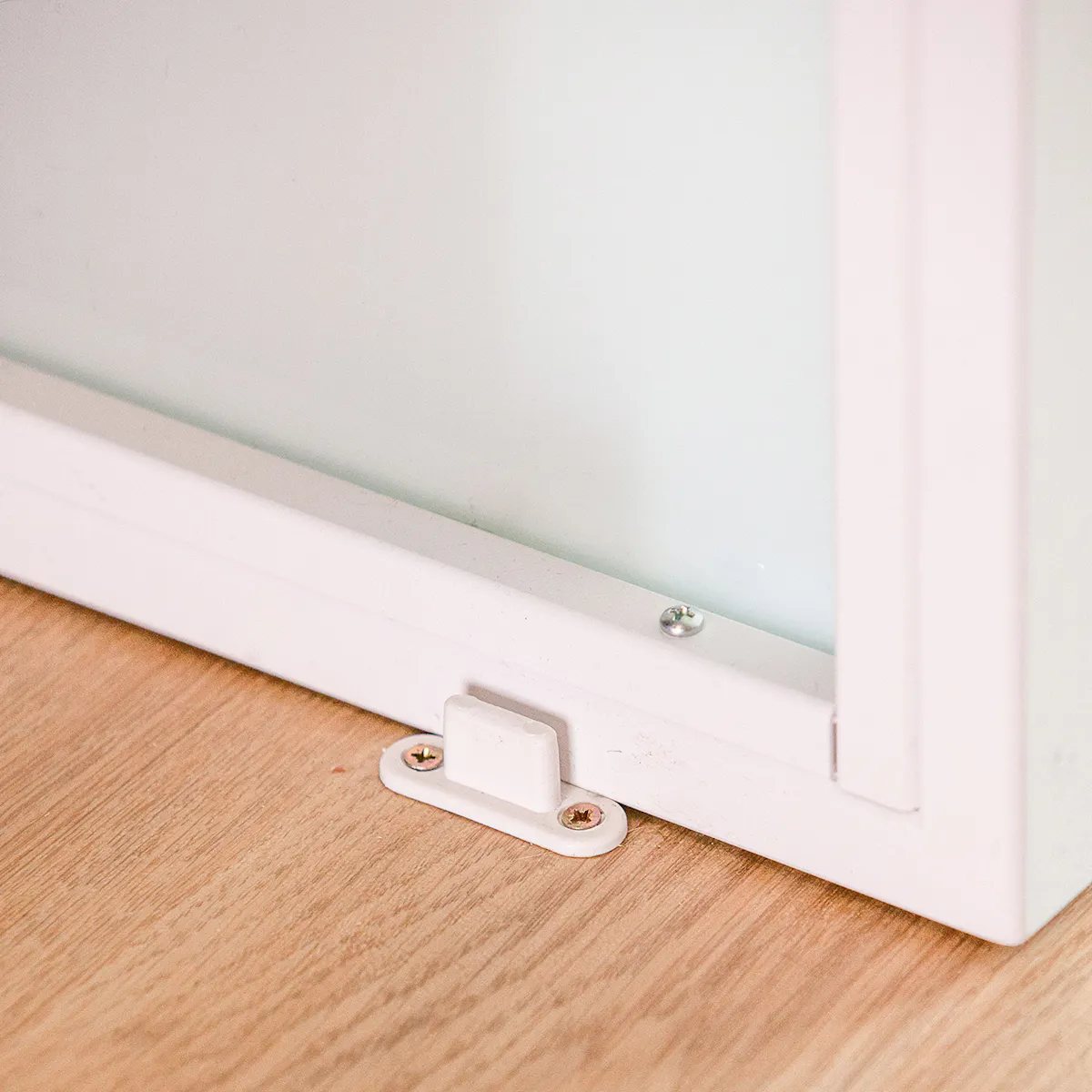 Detail of white floor guide at bottom edge of white sliding door mounted on wooden floor