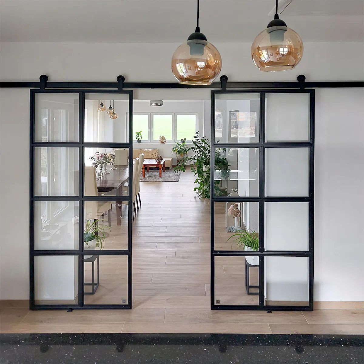 Black industrial sliding doors separate kitchen from living room; modern interior with classic elements and natural light