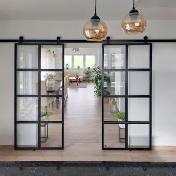 Des portes coulissantes industrielles noires séparent la cuisine du salon ; un intérieur moderne avec des éléments classiques et de la lumière naturelle.