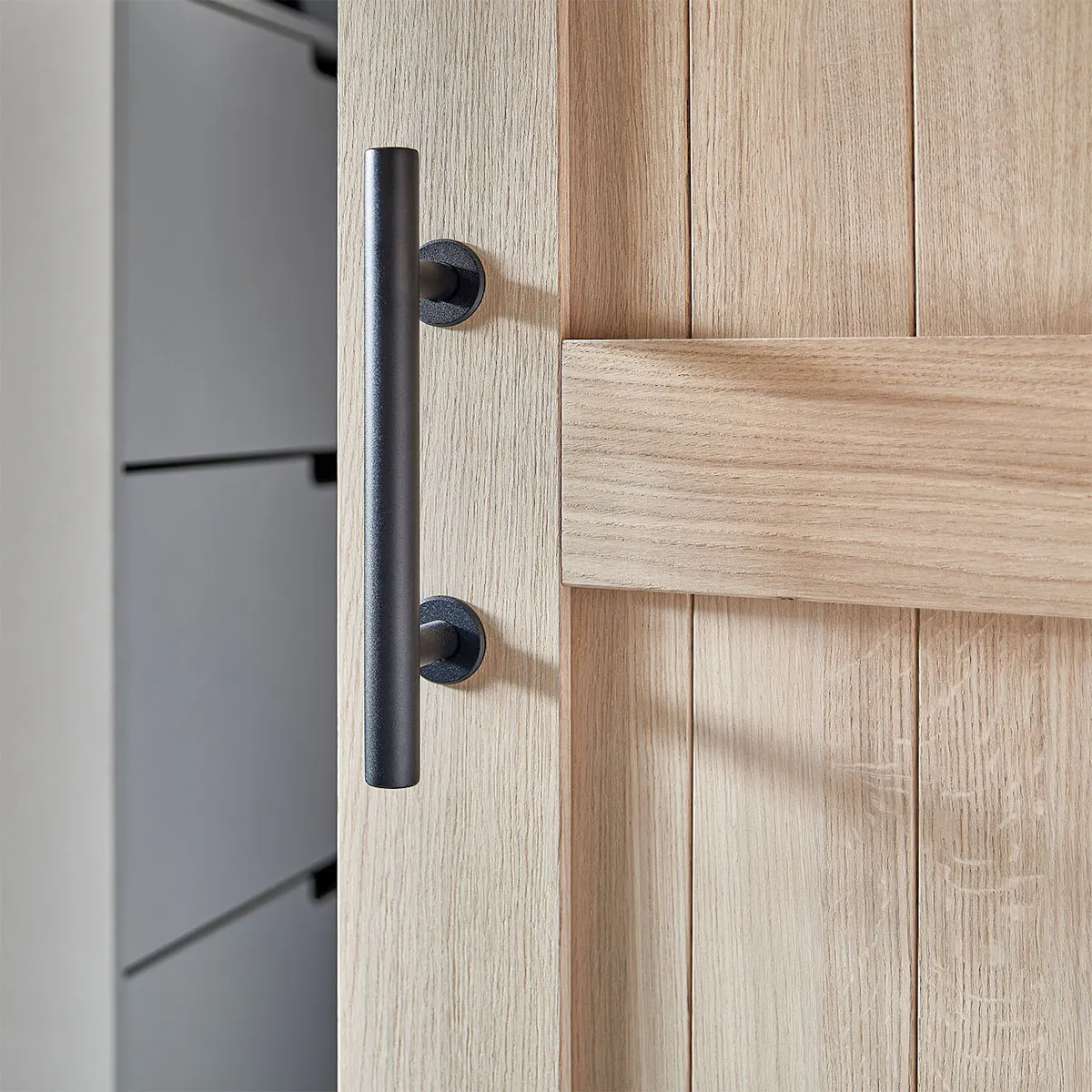 Detail of a black handle for an oak sliding door. The handle, shaped like a straight, matte tube, emphasizes the modern, minimalist style.