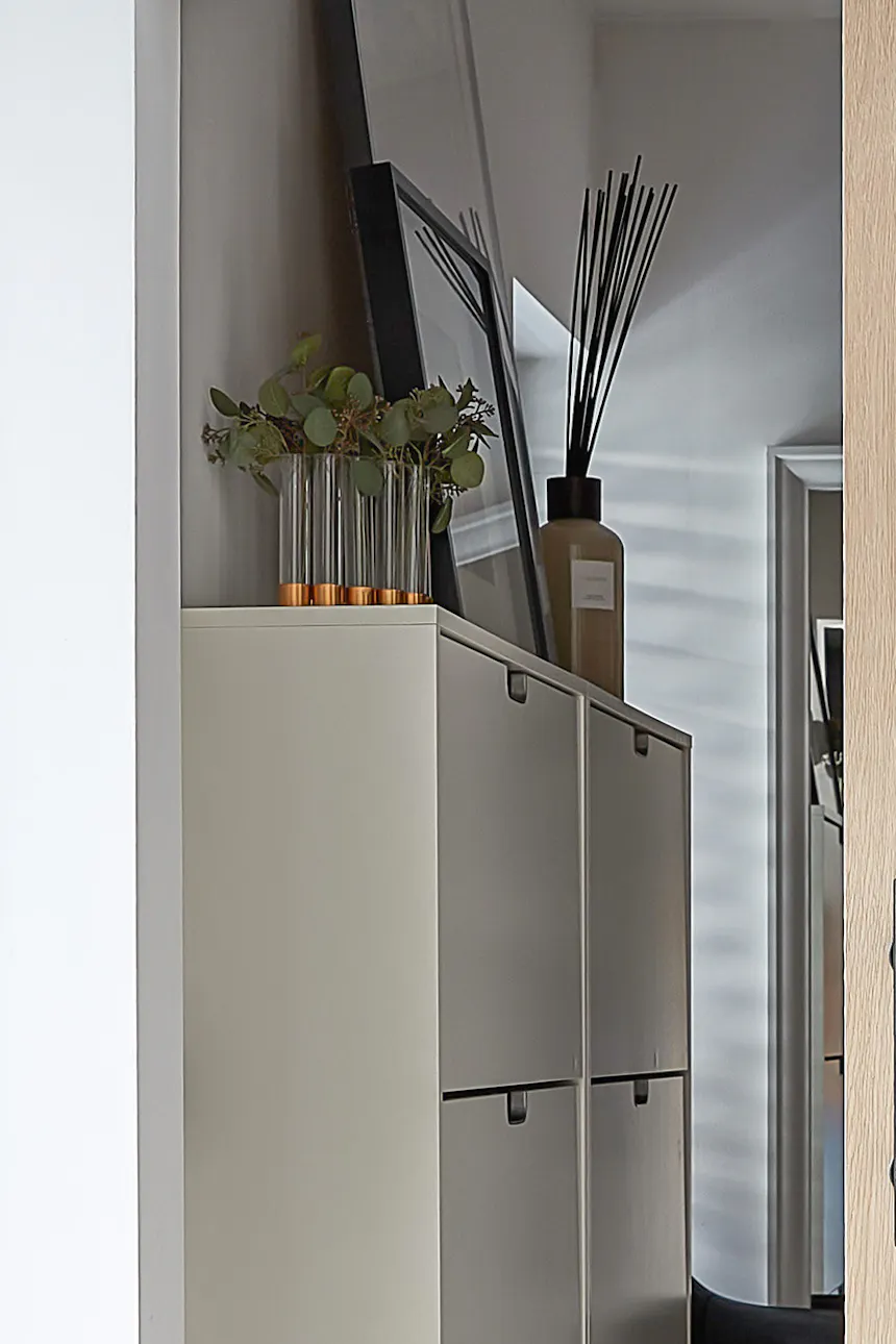 Details of the walk-in wardrobe's interior, visible through the ajar oak door. Stylish decorations sit atop a white shoe cabinet: a vase of herbs and a fragrance diffuser, lending the space a cozy and elegant feel.