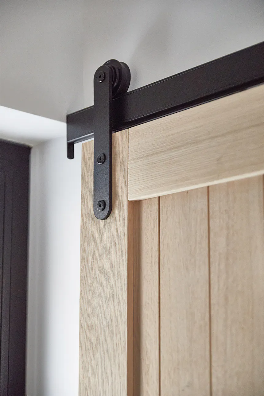 A close-up of the black sliding system (hardware) and the upper part of the oak door. The black system contrasts with the natural, light wood of the oak door, creating a harmonious blend of industrial and natural style.