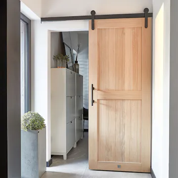 Un élégant vestibule avec des portes coulissantes en bois menant à un dressing. Des portes en chêne naturel avec quincaillerie noire, un grand pot de fleurs et un meuble à chaussures créent un espace fonctionnel et élégant.