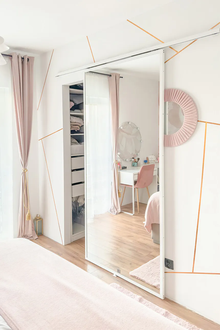 Bedroom with open dressing room; mirrored doors and pink velvet curtains; view of a white vanity