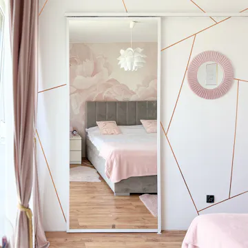 Chambre moderne dans les tons rose poudré et gris ; grand miroir sur la porte coulissante ; papier peint avec des roses derrière le lit ; lignes géométriques dorées sur le mur.