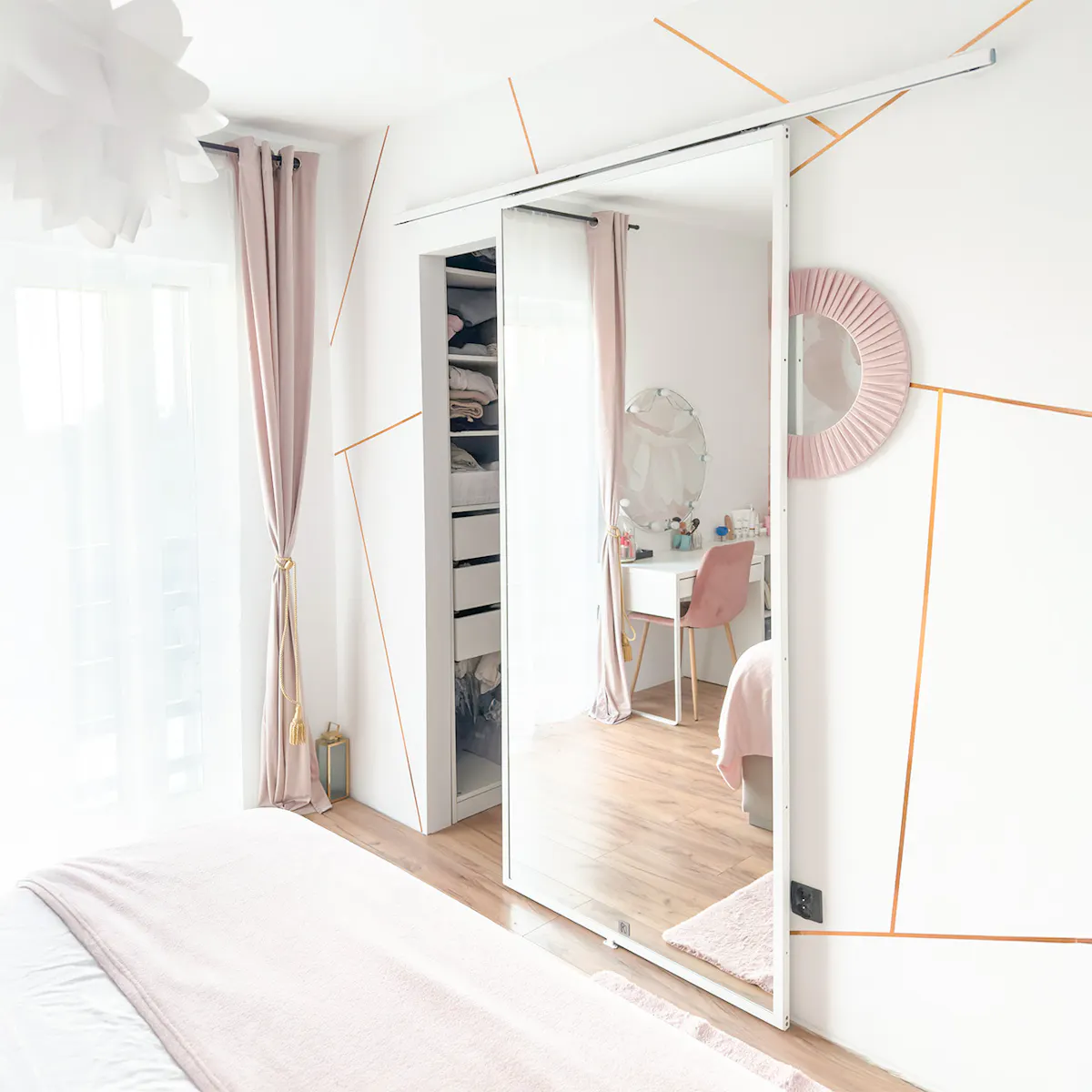 Chambre à coucher rose et grise ; un grand miroir sur la porte coulissante agrandit visuellement l'intérieur ; coiffeuse et rideaux clairs.
