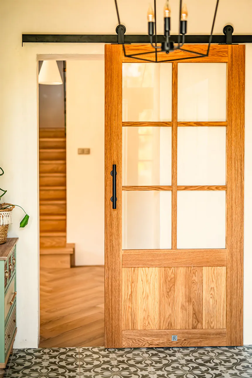 Oak barn-door style sliding door with glass insert and divided lights separating mudroom from hallway in modern farmhouse design