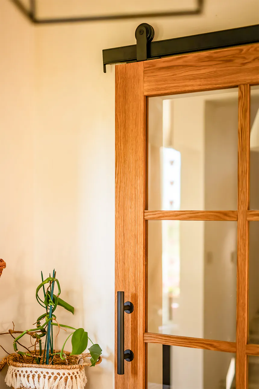 Partial view of oak sliding door with black vertical metal handle and divided-light glass panel
