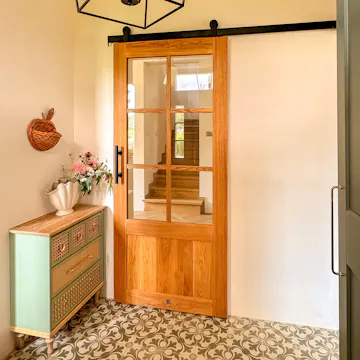 Portes coulissantes vitrées en chêne dans un vestibule aménagé avec une commode vert sauge et des carreaux de ciment à motifs.
