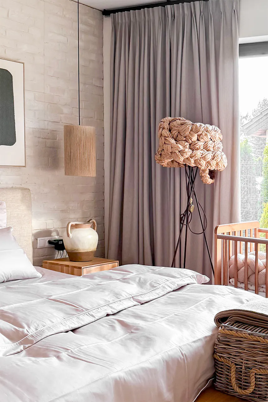 A cosy corner in the bedroom with a cot, a linen curtain and a mood-lighting lamp with an organic shape. In the background, a white brick wall.