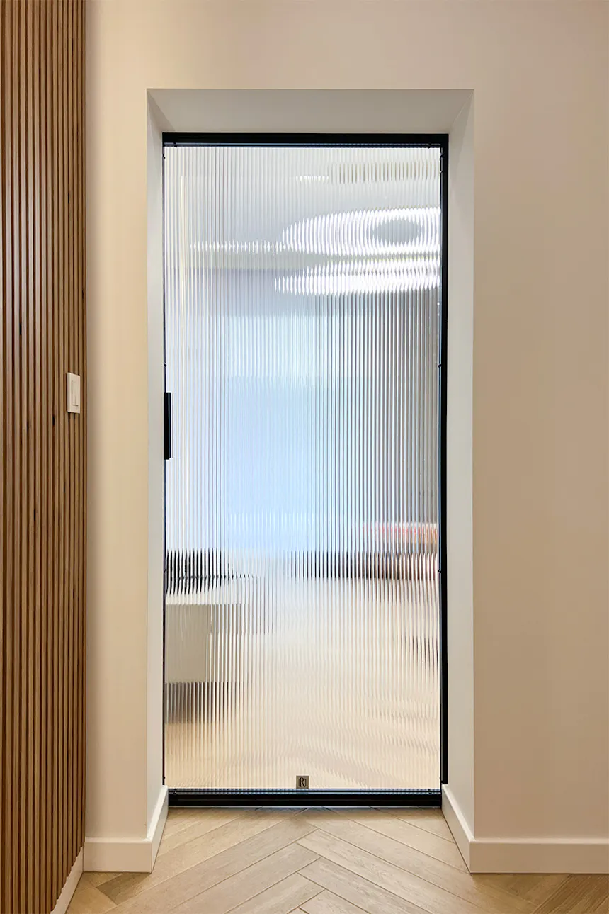 A minimalist hallway with sliding doors; a view from the corridor towards the living room through a fluted glass panel.