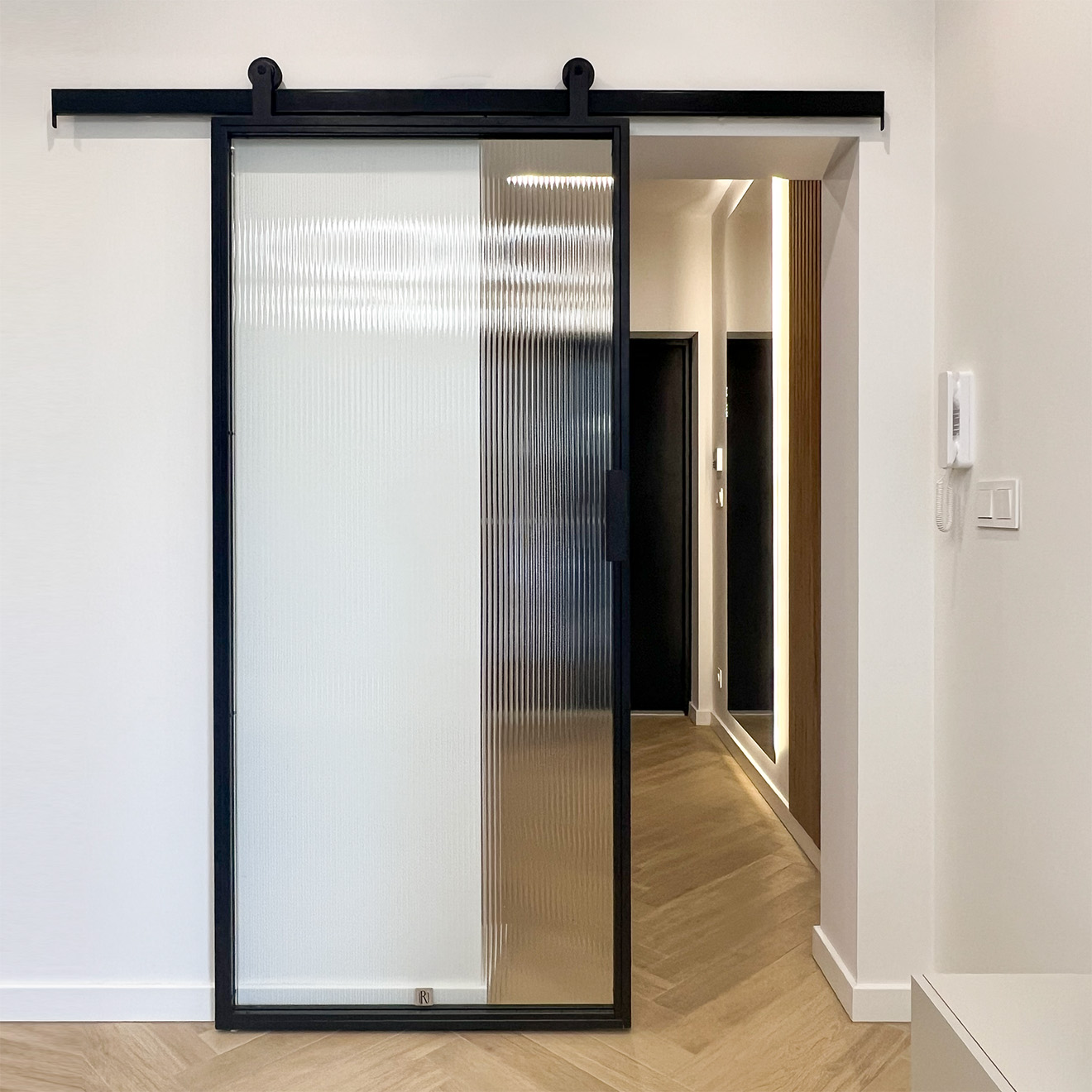 Black sliding doors with fluted glass, looking into the hallway with wooden slats and modern lighting.