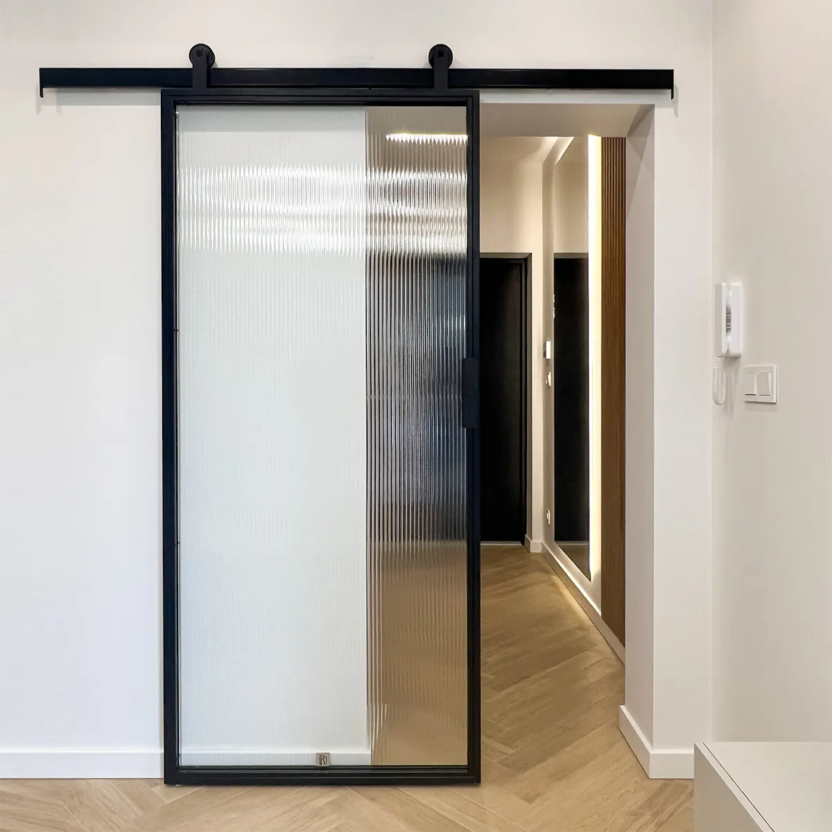 Black sliding doors with fluted glass, looking into the hallway with wooden slats and modern lighting.