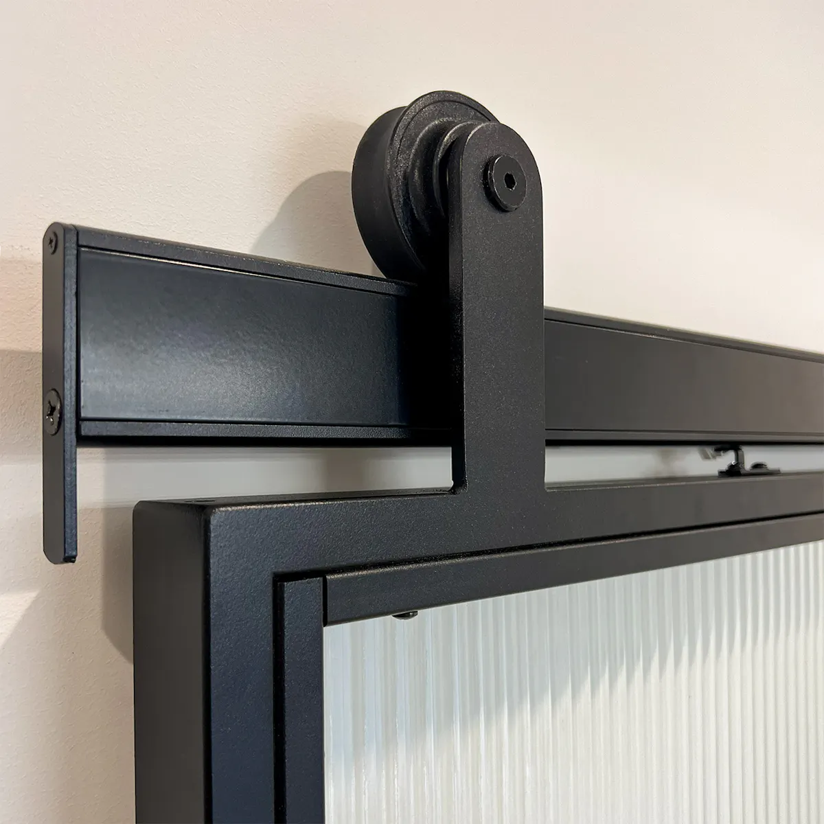 The black Reno Smart sliding system on a door with fluted glass, close-up of the roller and sliding track.
