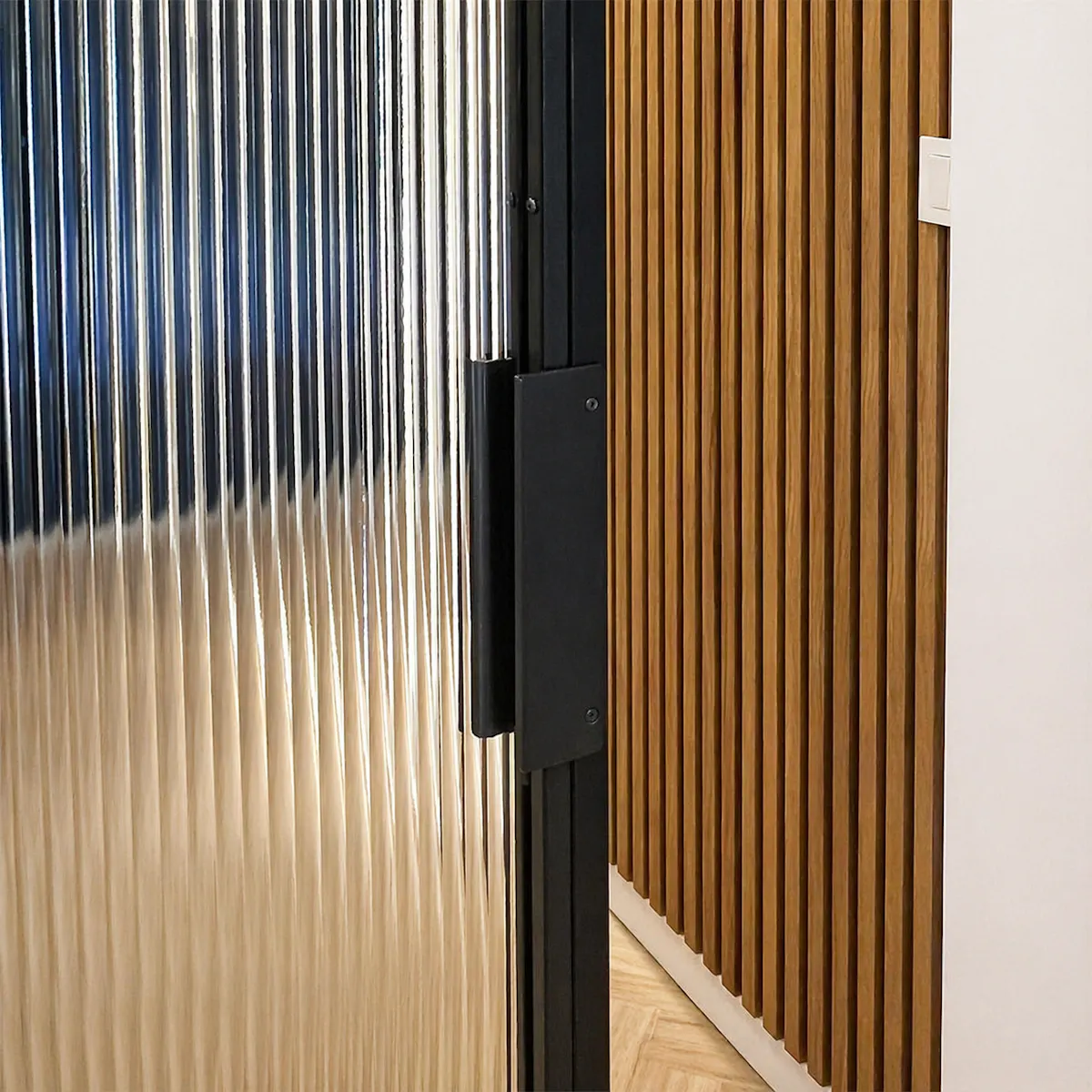 A close-up of the black vertical handle on the steel frame of a sliding glass door.