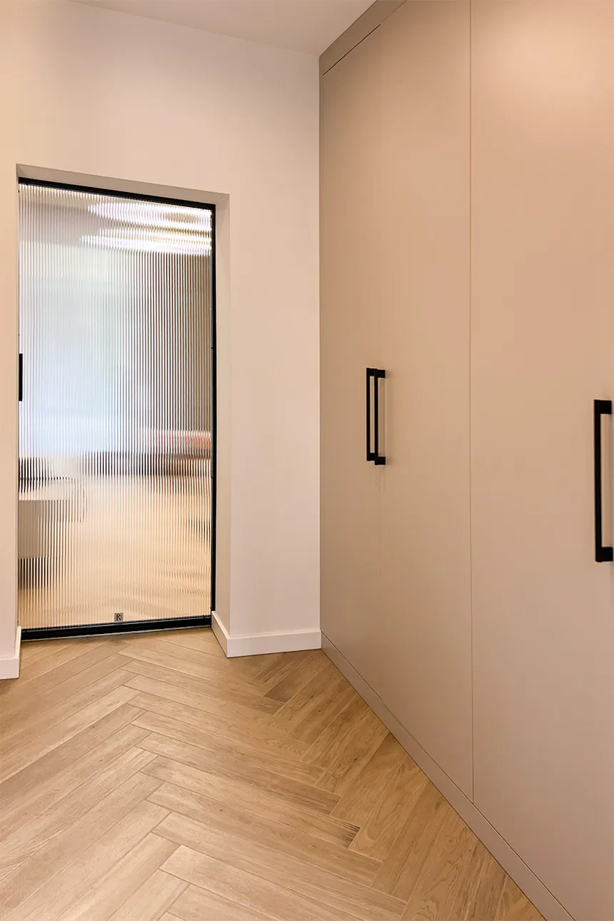A bright hallway with a beige wardrobe and minimalist-style sliding glass doors.