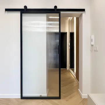 Des portes coulissantes noires en verre cannelé donnant sur le couloir, avec des lattes en bois et un éclairage moderne.