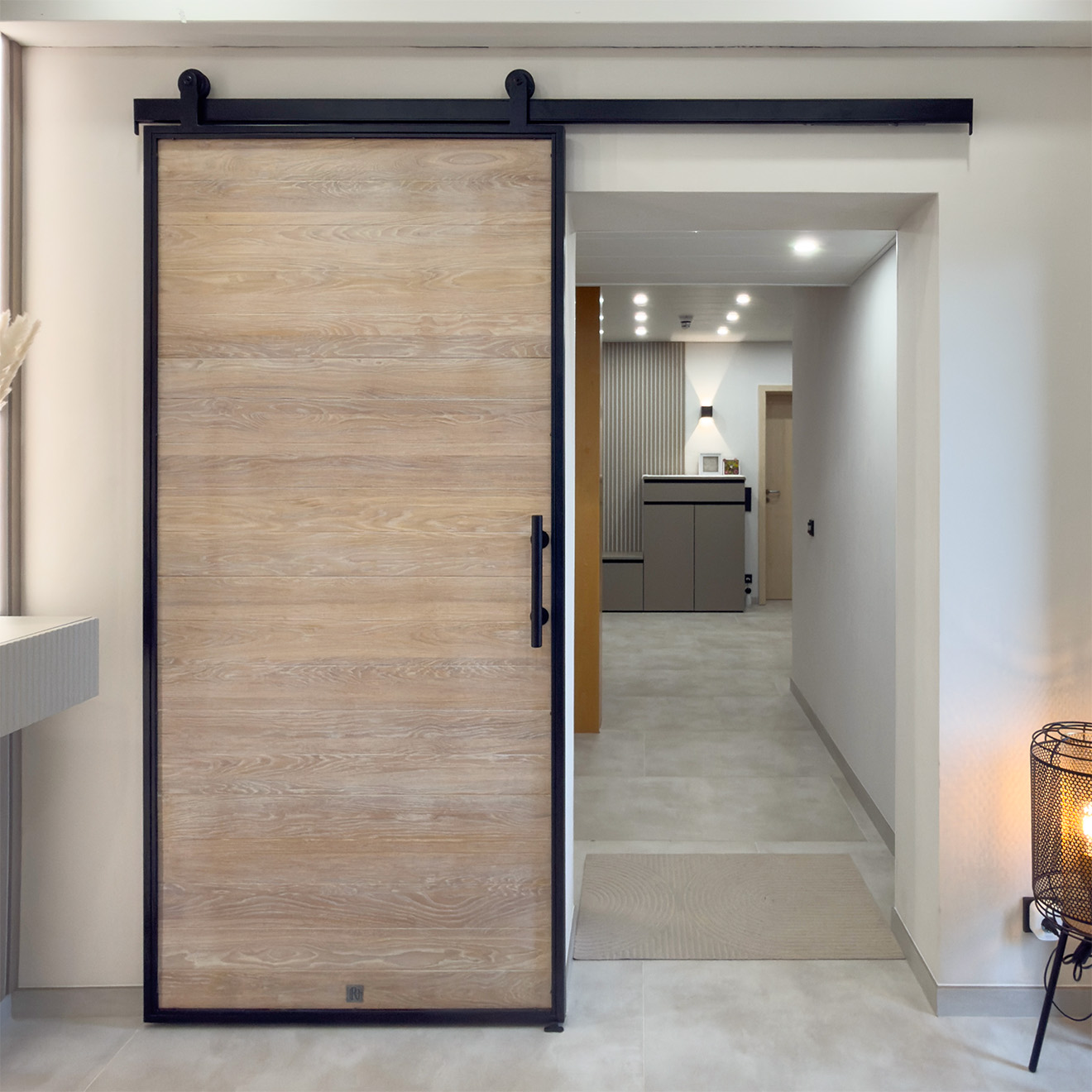A bright entrance hall with oak sliding doors set in a black metal frame, leading to the hallway.