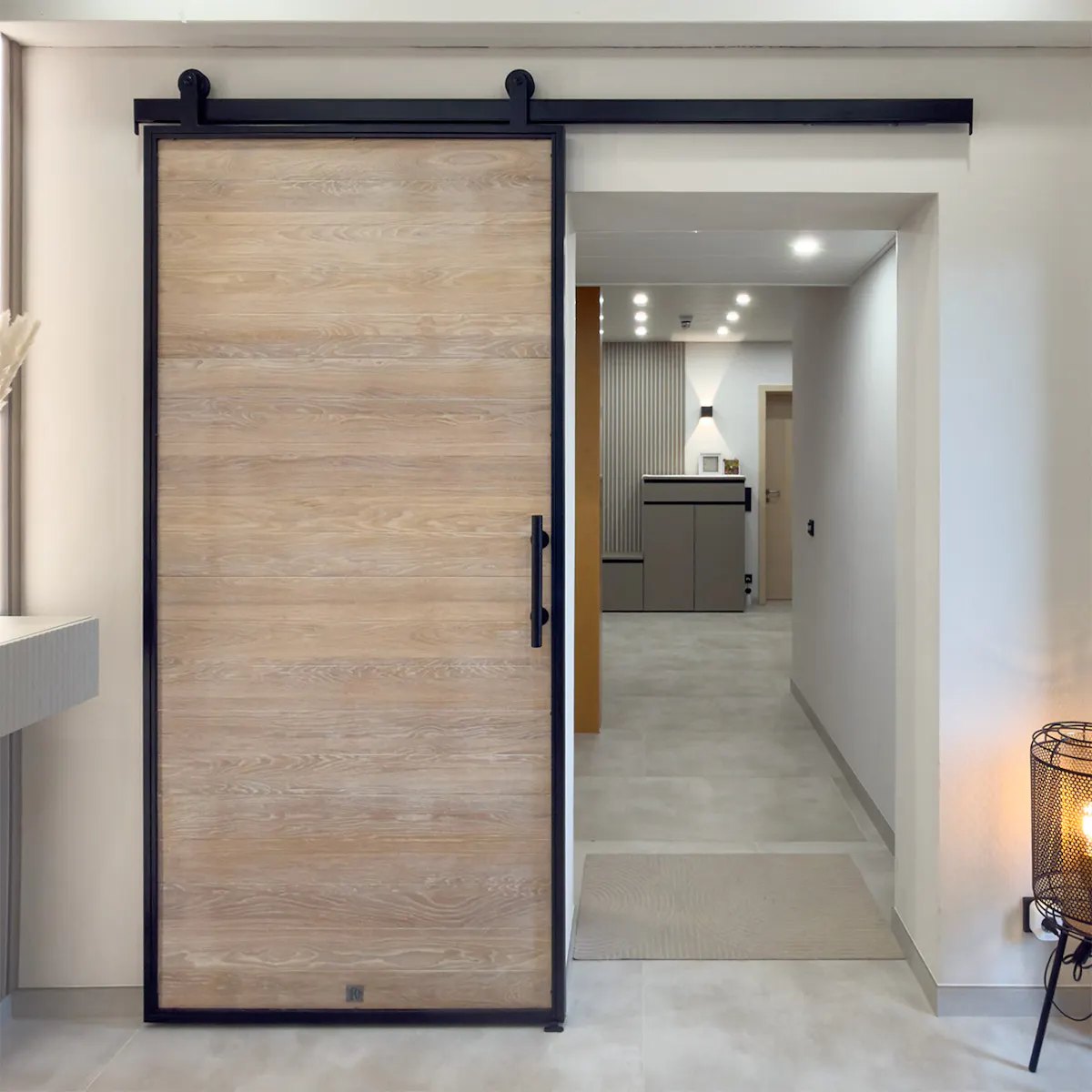 A bright entrance hall with oak sliding doors set in a black metal frame, leading to the hallway.