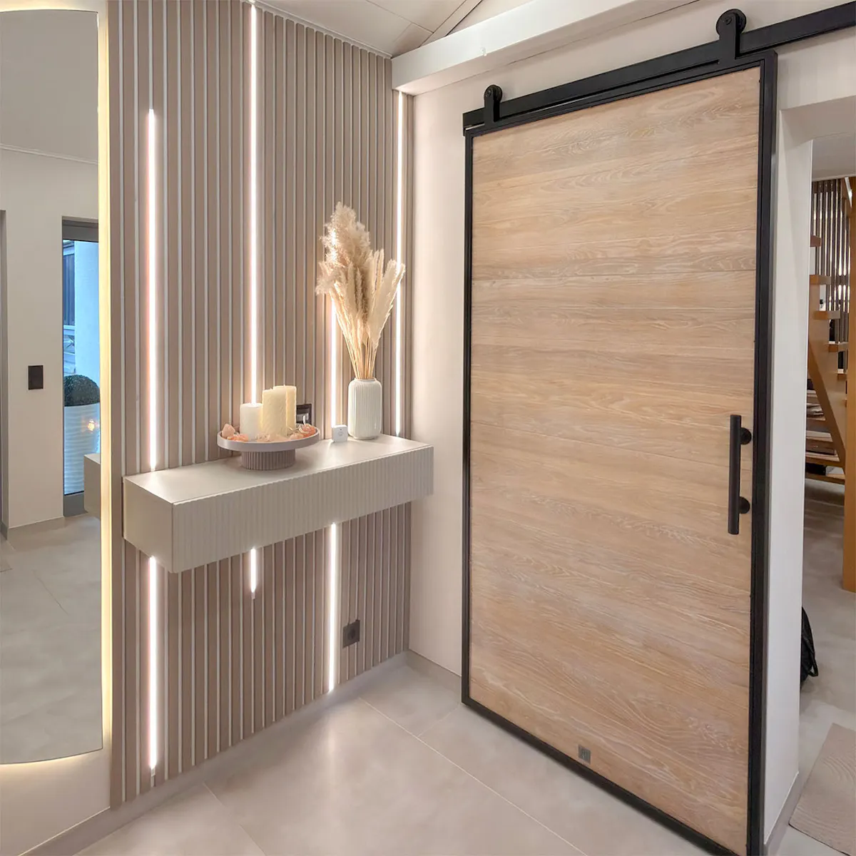 A modern entrance area in a warm minimalist style. On the wall, decorative slats with vertical LED lighting and a wall-mounted console table, alongside oak sliding doors in a loft style