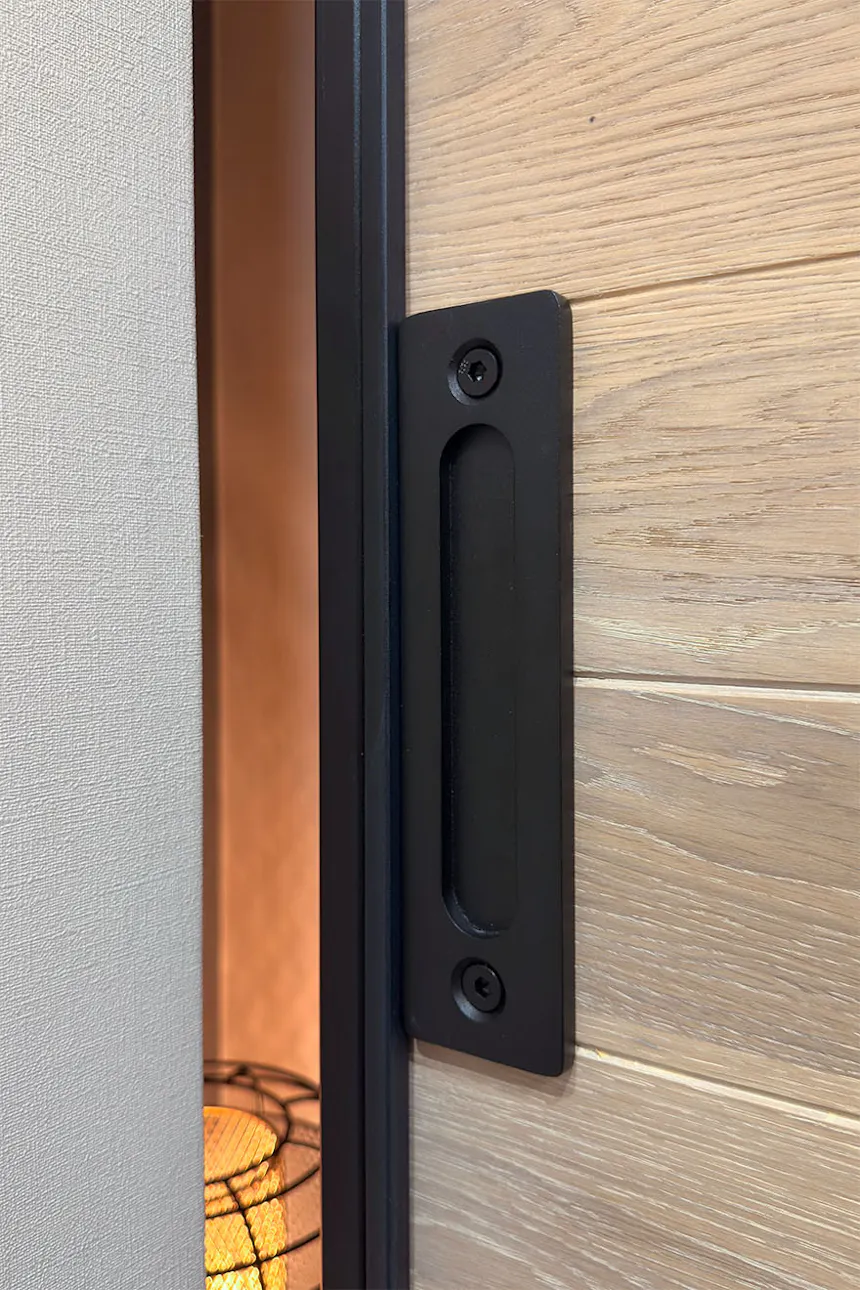 A detail of a black recessed handle on an oak sliding door.