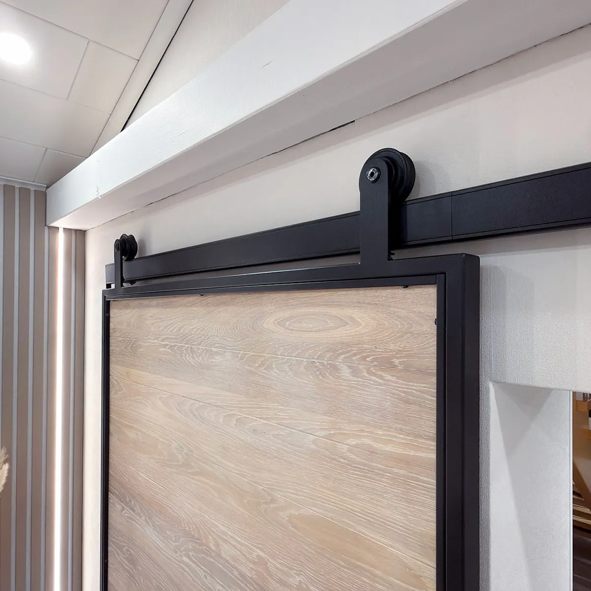 Sliding system Smart in black – a close-up of the rollers, the sliding track and the loft-style fitting fitted onto the whitewashed oak door.