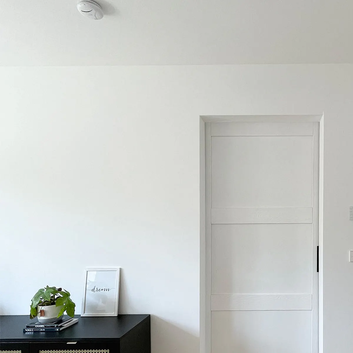 Black low rattan dresser against white wall, white solid wood sliding door