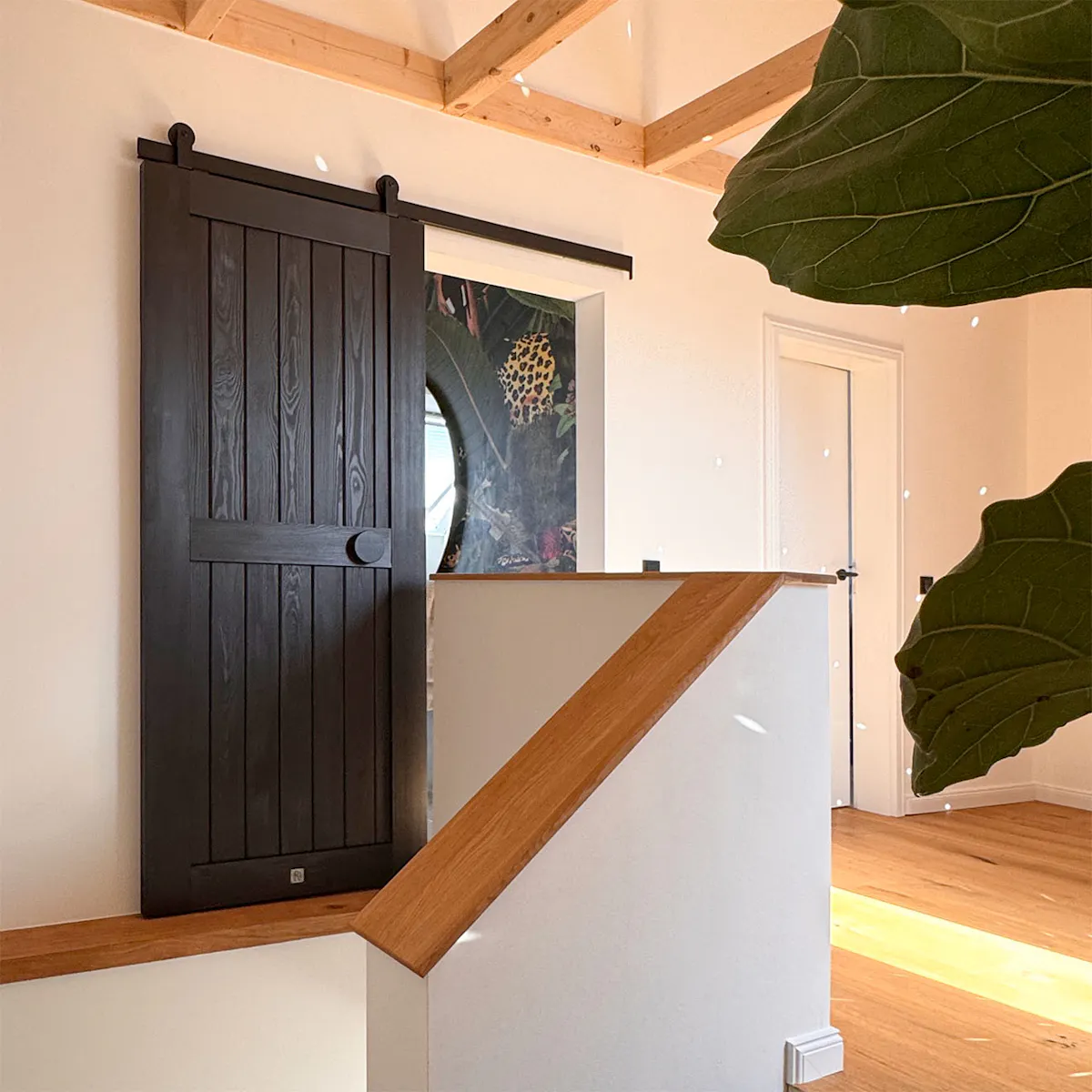 A black sliding door in the corridor in the loft, right next to the wooden staircase banister.