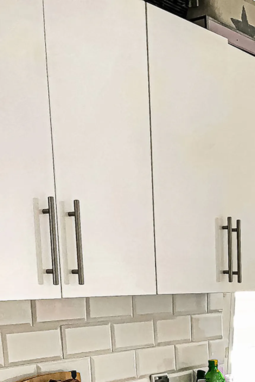 sliding doors in a small apartment, white kitchen cabinet with a wooden top, black kitchen accessories, white tiles on the kitchen wall