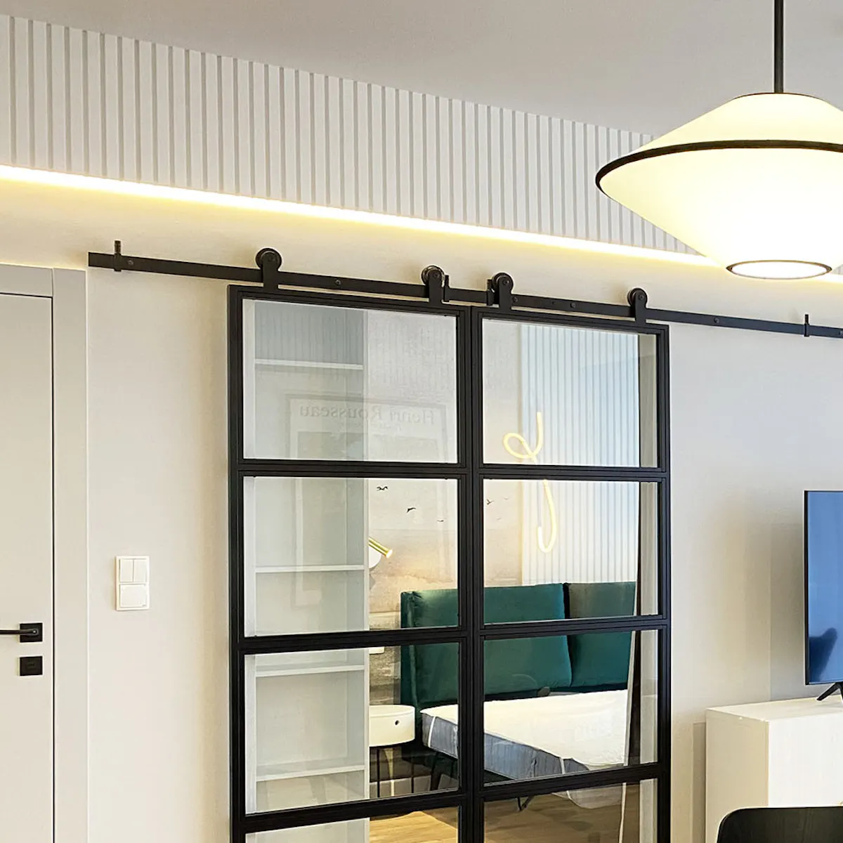 Double metal glass sliding doors separating bedroom from living room in modern apartment, designer lighting, bed with upholstered headboard, white walls and linear molding