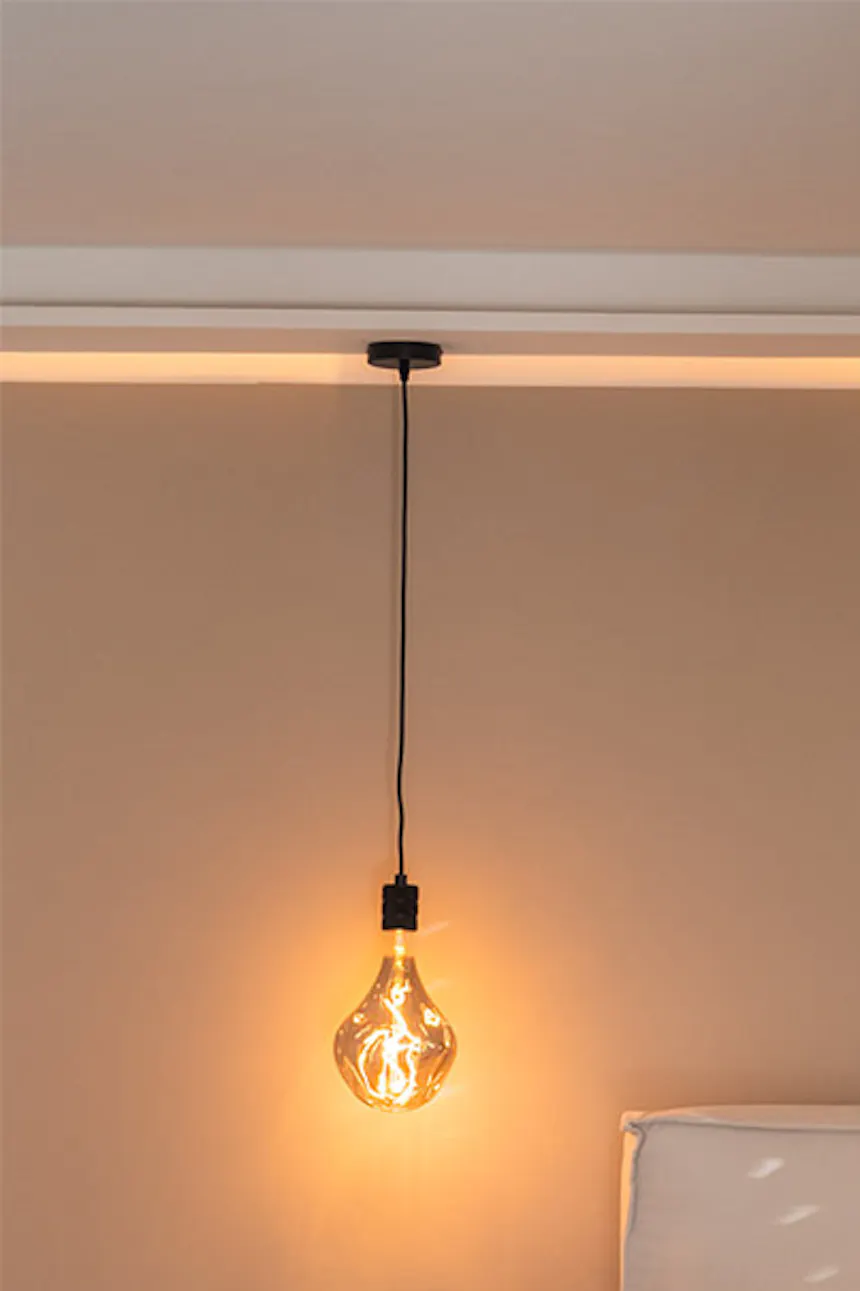 Hanging bulb lamp, small black nightstand, bed in beige bedroom setting