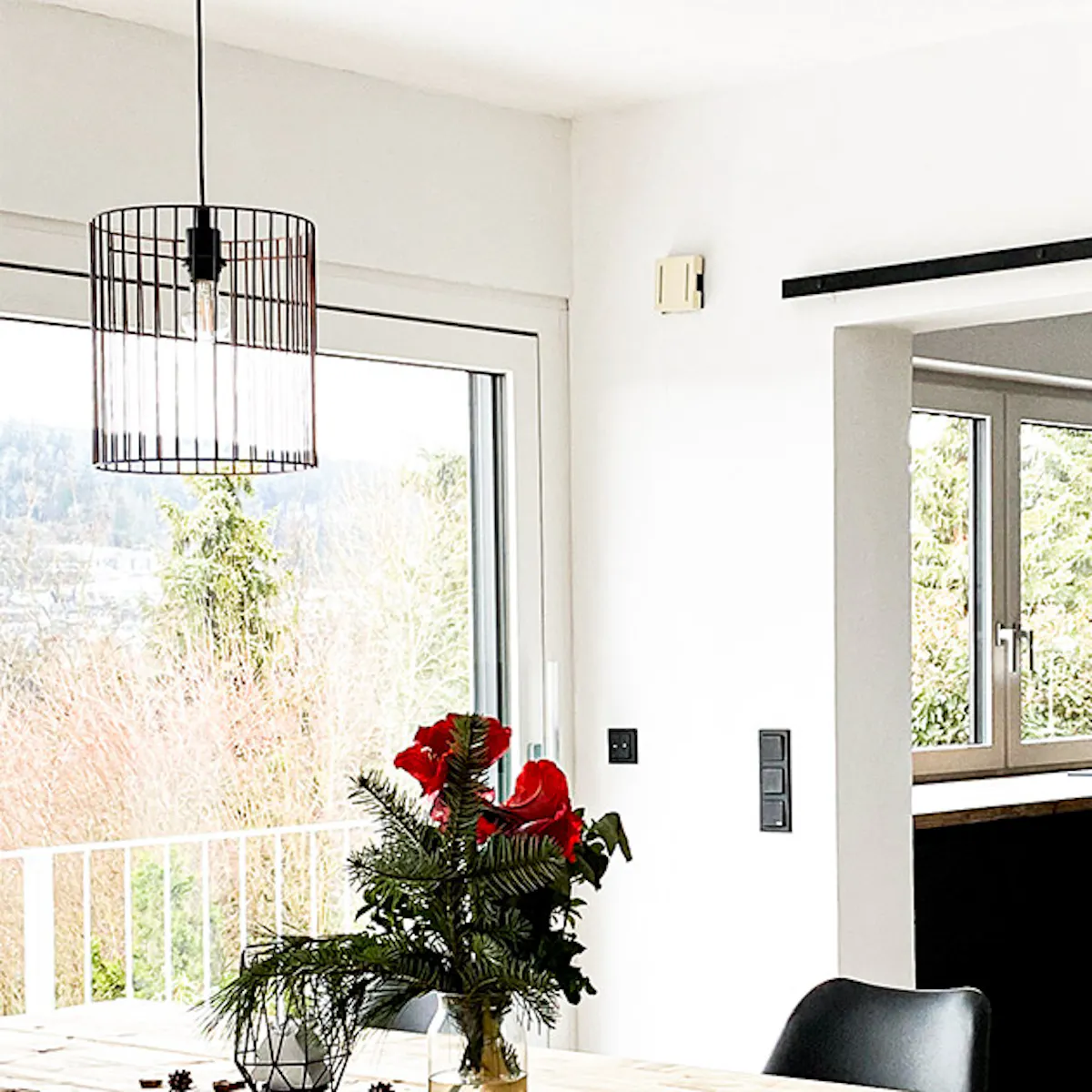 wood and metal in dining room, wooden sliding door, wood and metal dining table, large green plant in basket, black chairs on metal legs, table and chairs in dining room, door to kitchen