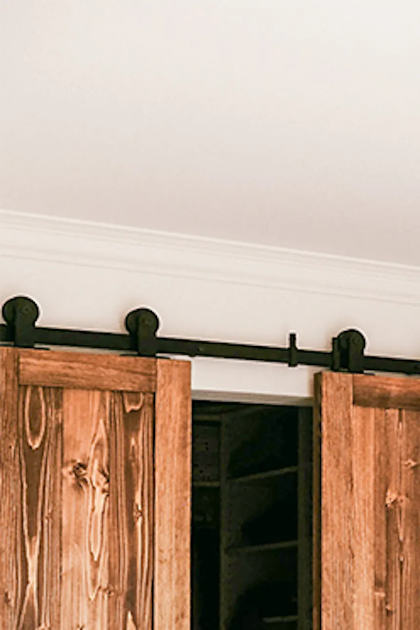 couvre-lit beige et oreillers décoratifs dans la chambre avec une petite armoire cachée derrière des portes coulissantes