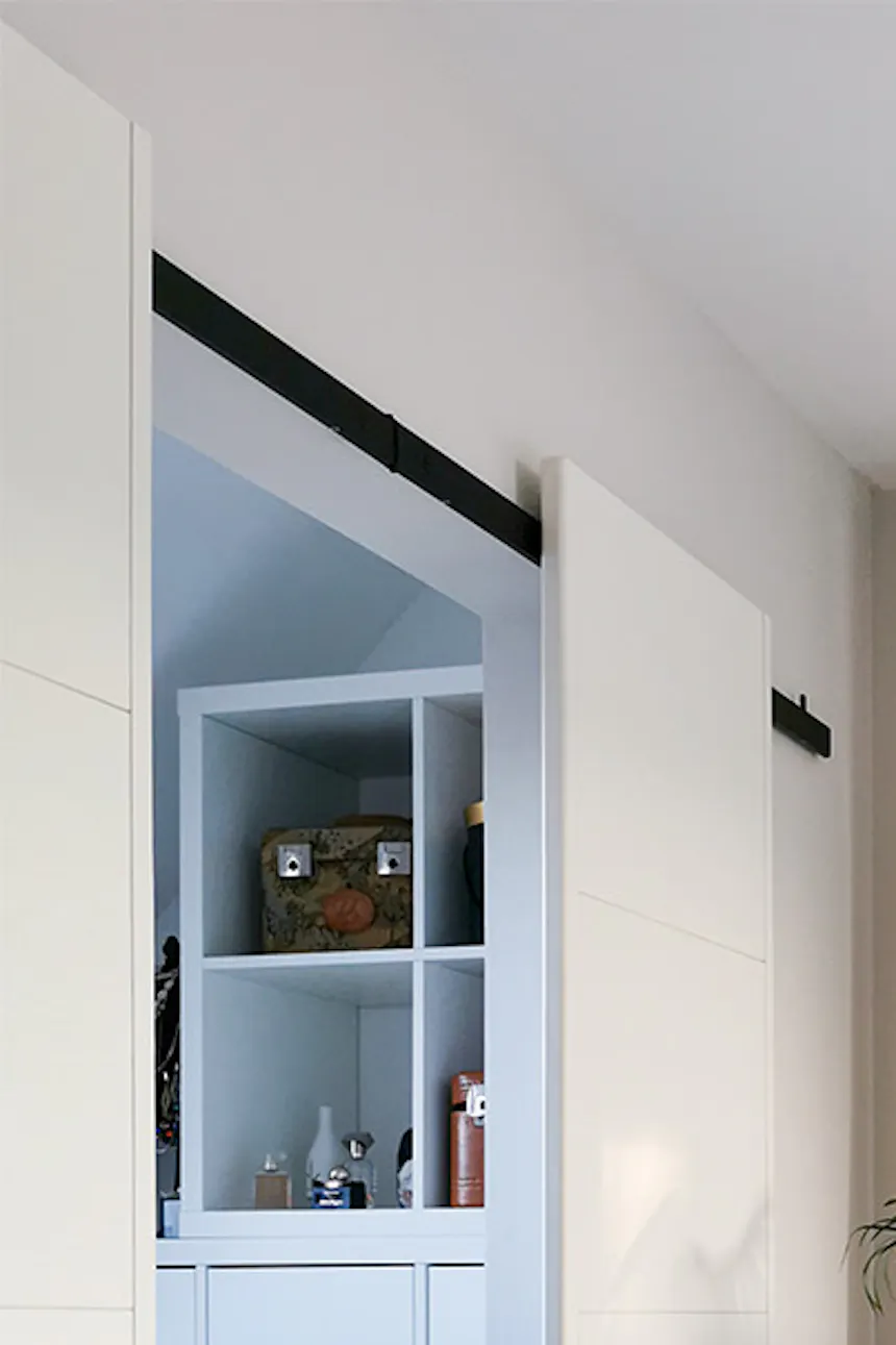 une grande plante dans un pot tressé à côté d'une porte coulissante blanche menant à un petit dressing