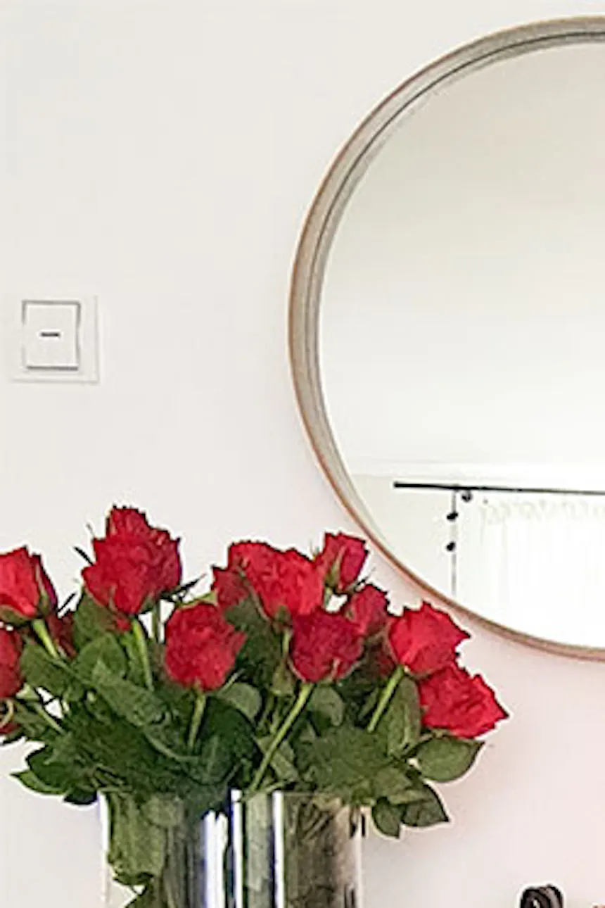 white chest of drawers with wicker baskets for bedding in a Scandinavian interior, live flower decoration in the bedroom, white walls and white furniture in the bedroom, braided rug