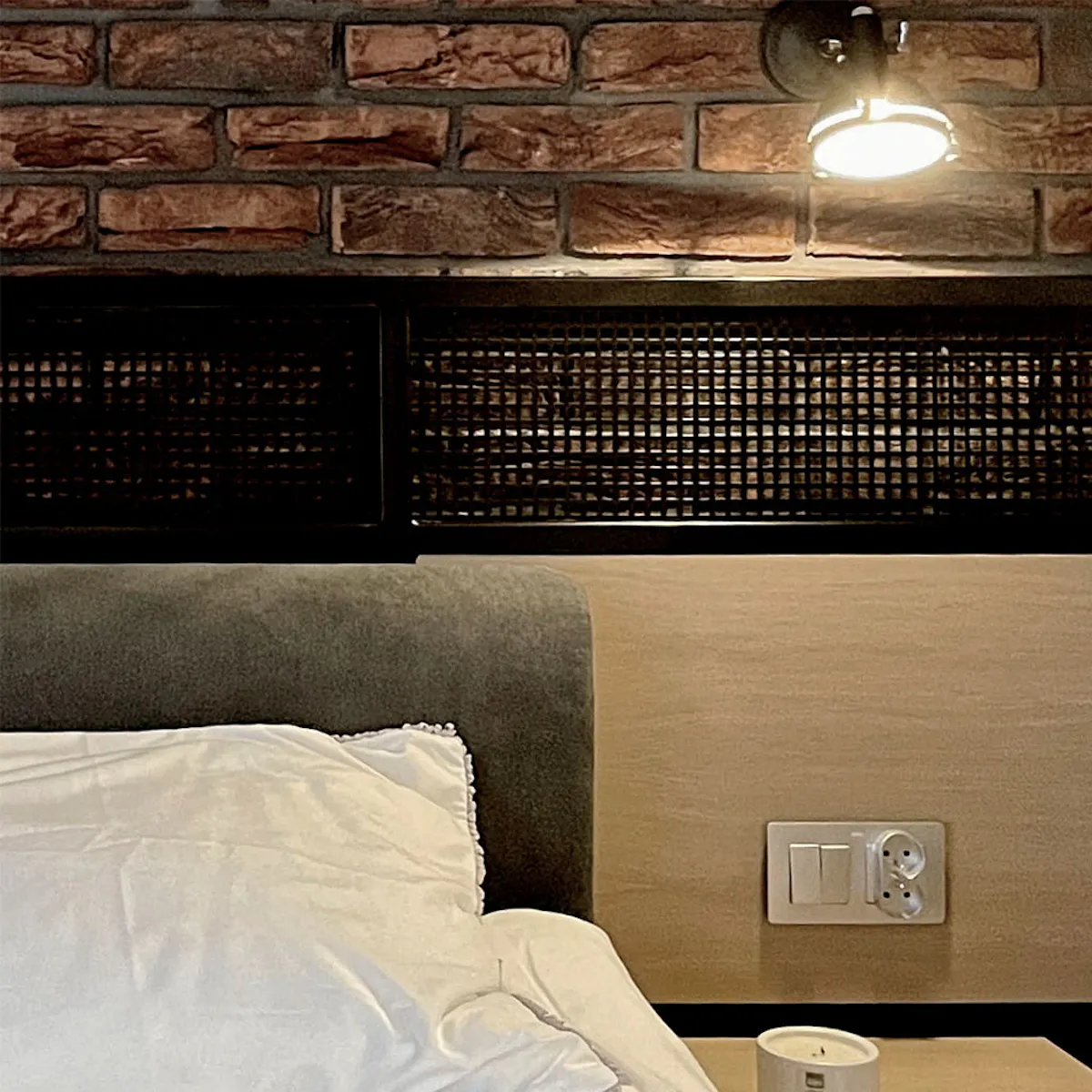 Red brick wall in industrial bedroom with loft nightstand and decorative metal plate behind bed