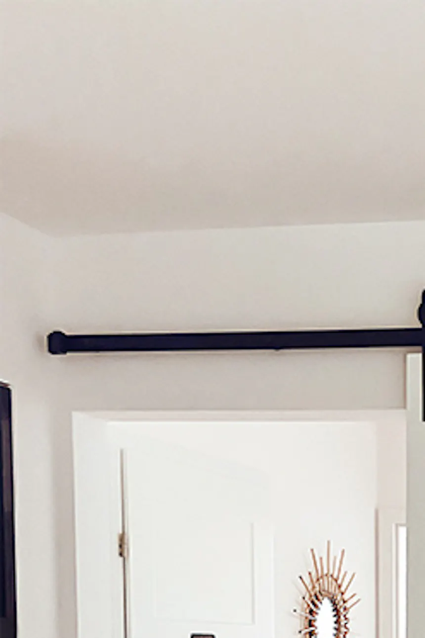 white sliding door in the entrance to the bedroom, white walls and wooden floor in a natural bedroom, bamboo lampshade, colourful, decorative rug in front of the bed