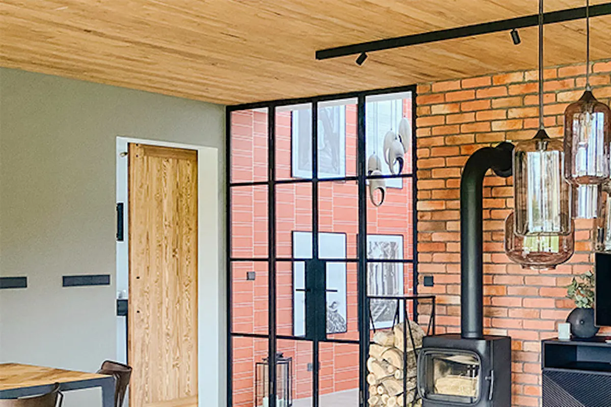 Industrial loft-style living room, microcement floor, wooden ceiling, black metal elements, black fireplace, glass and steel lamp, glass coffee table, brick wall