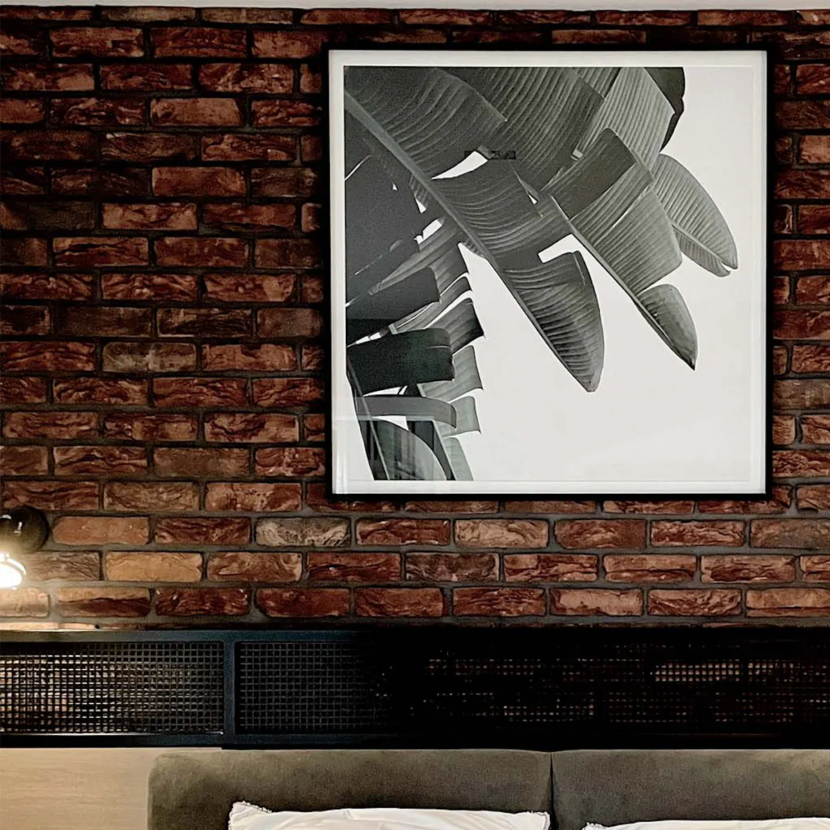 Framed black and white poster on red brick wall in industrial bedroom with industrial decor