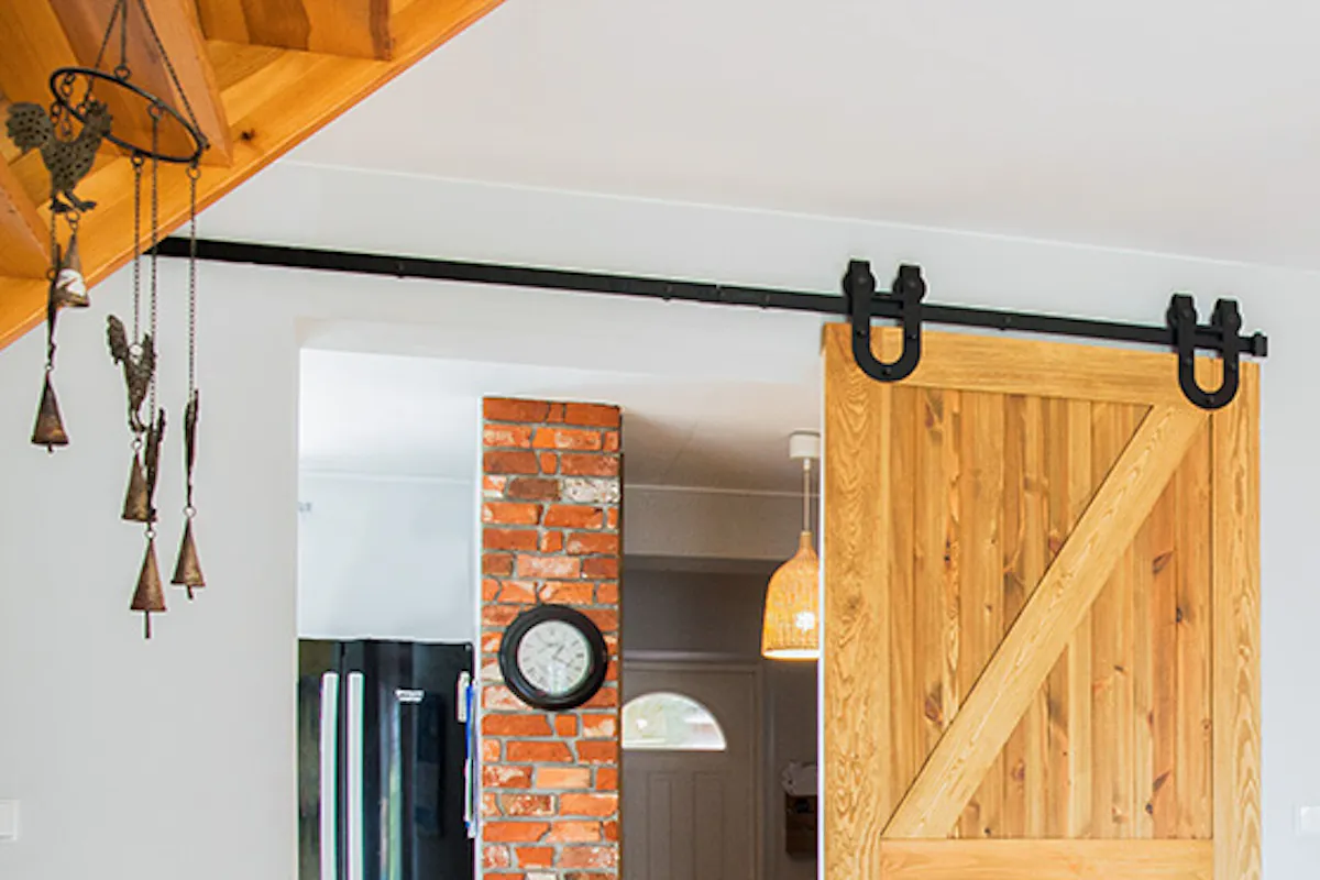 rustic wooden door, brushed wood sliding door, barn door, sliding door with a 'horseshoe' system, sliding door to the kitchen, large blue sofa in the living room, brick on the wall