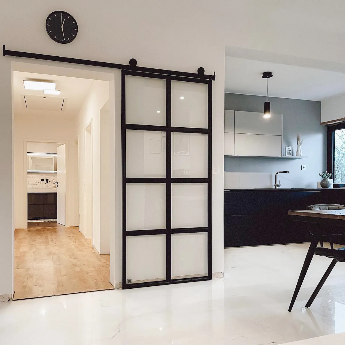 Glass sliding doors, metal door with clear glass, black and white open kitchen, black clock on white wall.