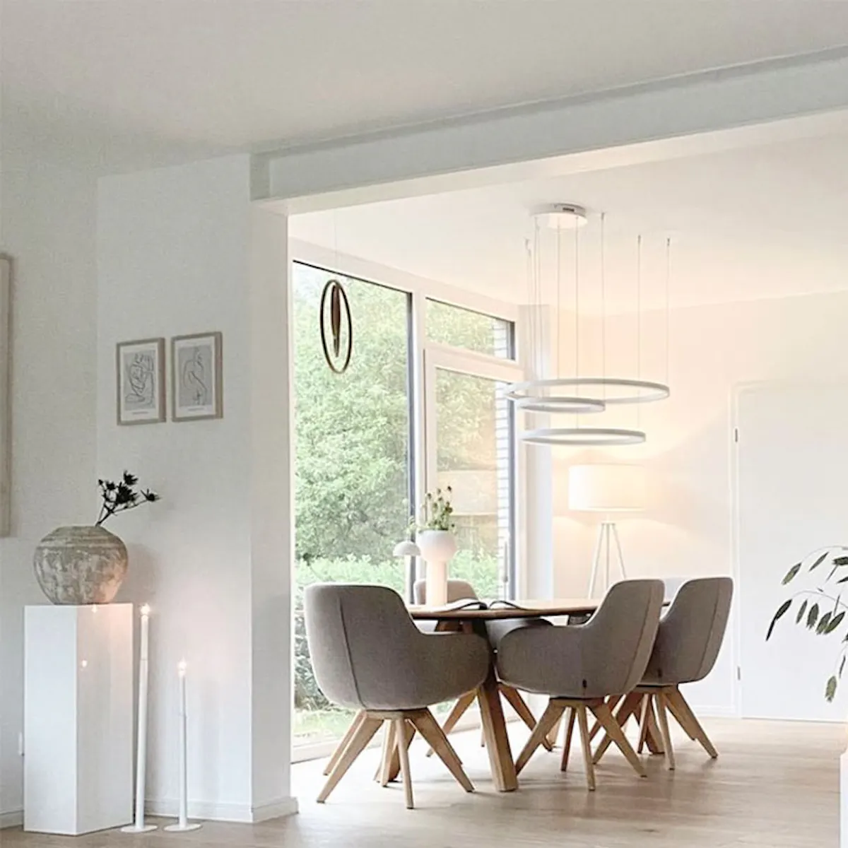 Open living room connected to dining room, large comfortable dining chairs, round Nordic style table, vases with plants decorating table