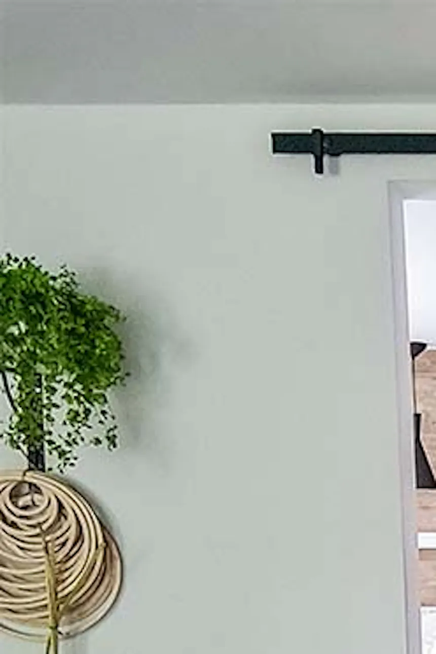 wooden sliding door in the bedroom entrance, wicker chair with decorative pillows, braided round jute rug, floral decorations in a wicker basket, white bed in a bedroom in a Scandinavian interior, black pendant lamps over a white bed