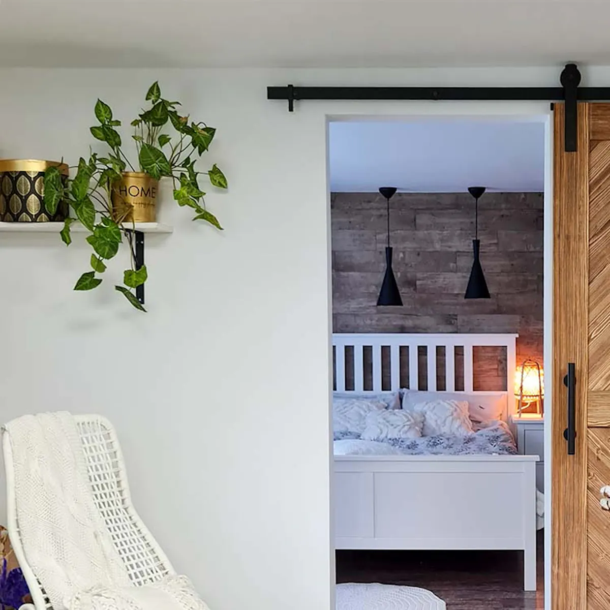 wooden sliding door in the entrance to the bedroom, white rocking chair, black sliding system, white large bed in a Scandinavian interior, black lamps hanging over a white bed