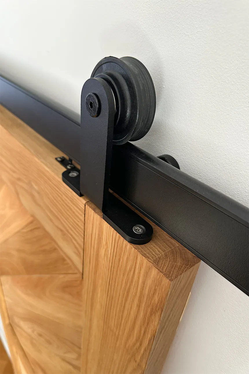 A close-up of the black Smart sliding system roller mounted on the top edge of an oak door.