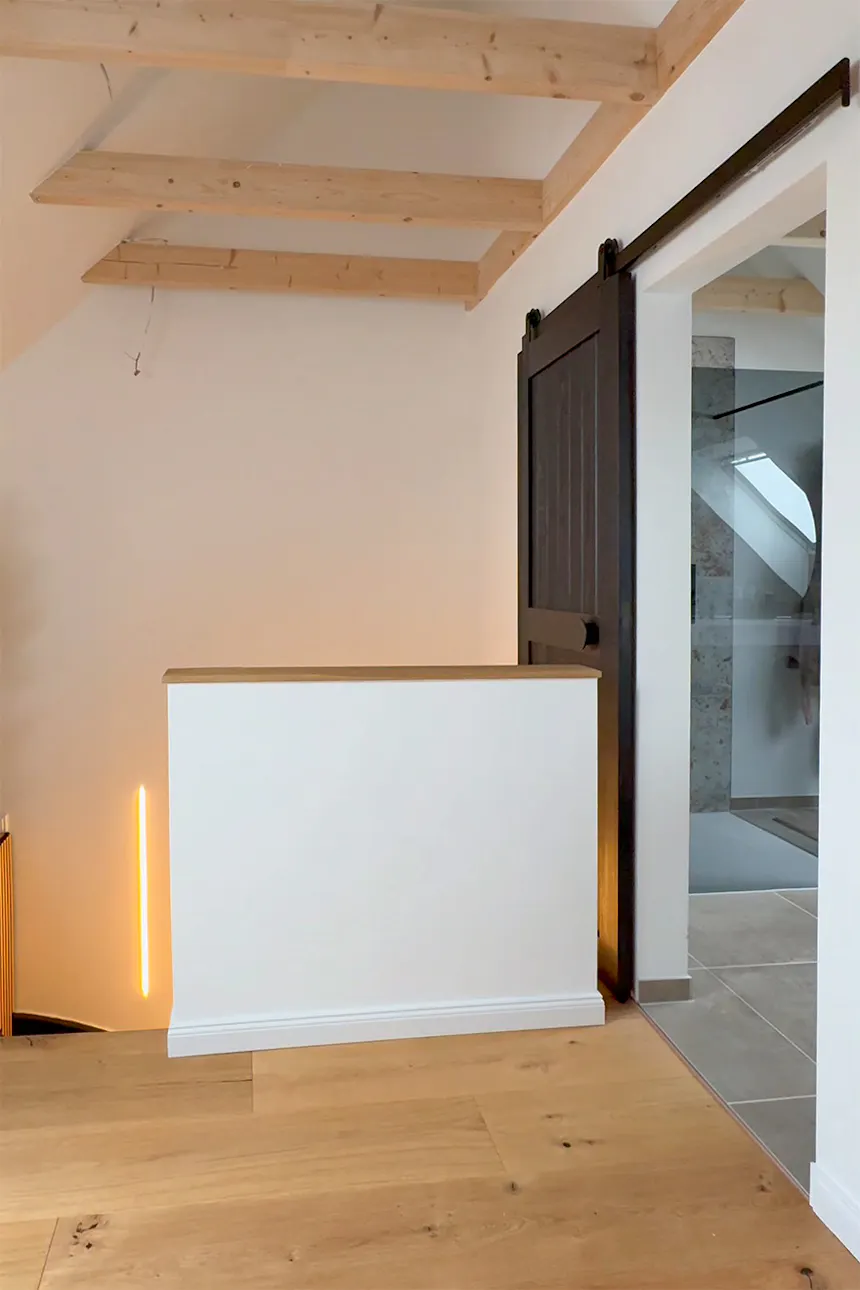 An open black sliding door in the circulation area in the loft, revealing the passageway to the bathroom with its glass shower cubicle.